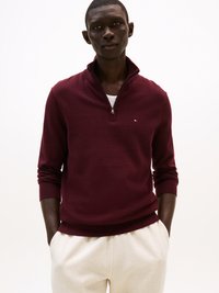 Bordo zip-up pulover s visokim ovratnikom, teksturiranom tkaninom i rebrastim manžetama, nosi se preko svijetlo obojenog košulje i uparen je s bež hlačama.