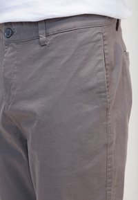 Close-up van grijze casual broeken met knoop en tailleband, gedragen met een ingestopt wit shirt.