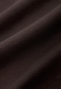 Gros plan sur un tissu marron foncé avec une texture tricotée fine et douce visible et de légers plis.