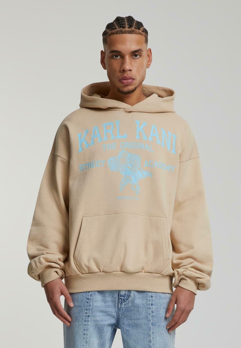 Felpa beige con cappuccio, testo blu e grafica di un'aquila, dotata di tasca frontale a kangaroo e polsini e orlo a coste.