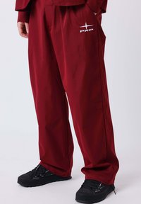 Pantaloni bordeaux a gamba larga con finitura strutturata, con logo PXP bianco e tasche laterali. Abbinati a sneakers nere dalla trama strutturata.
