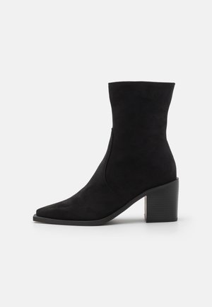 Bottines noires en daim avec un bout pointu, une texture lisse et un talon épais et texturé pour plus de stabilité. Détail de fermeture éclair sur le côté.