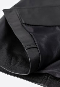 Chaqueta negra de cuero plegada que muestra la textura exterior suave y el detalle del tejido del forro interior brillante.