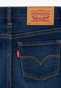 Sötétkék farmernadrág arany öltésekkel, bőr címkével, amelyen a "Levi Strauss & Co." felirat szerepel, és egy jellegzetes piros címkével a hátsó zseben.