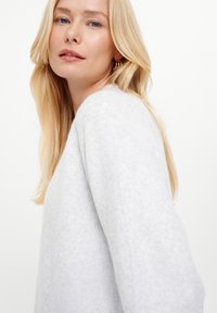 Maglione grigio chiaro a maglia con una vestibilità larga, scollatura arrotondata e maniche allungate. Tessuto morbido con leggere variazioni di colore.