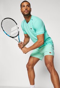 Mint green tennis outfit featuring a textured short-sleeve top and matching shorts, with logo accents and contrasting blue stitching.