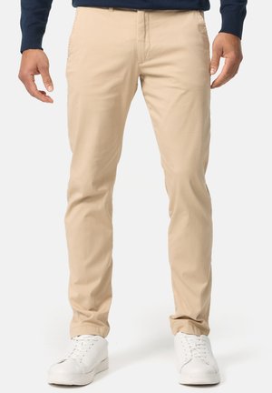 Khaki chinot valmistettu sileästä puuvillakankaasta, joissa on slim fit -leikkaus, tavalliset taskut ja ne on yhdistetty valkoisiin tennareihin rentoa ilmettä varten.