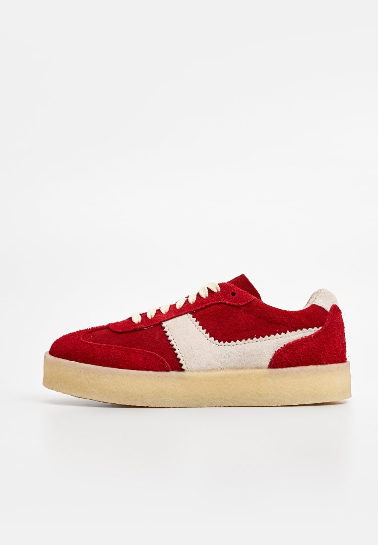 Baskets en daim rouge avec des accents crème, un bout arrondi et une semelle en caoutchouc beige. Présente des lacets à œillets et des détails de couture en zigzag.