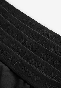 Svart elastisk midjeband med pr�äglad "NEXT"-text och hjärtmönster, designat för komfort och passform, med en mjuk, texturerad yta.