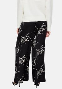 Schwarze Hosen mit weitem Bein und floralem Muster, das weiße und rote Akzente aufweist. Hergestellt aus leichtem Stoff mit glatter Textur.