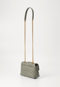 Ορθογώνια τσάντα χειρός από ήσυχο πράσινο δέρμα με ραμμένα κυματιστά σχέδια. Διαθέτει καμπύλη γκρίζα λαβή και χρυσή αλυσίδα.
