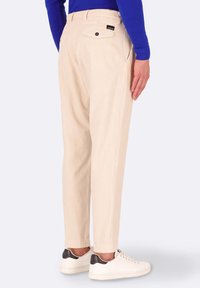 Pantaloni a costine beige con una vestibilità rilassata, dotati di tasca posteriore e cintura elasticizzata, abbinati a sneaker bianche.