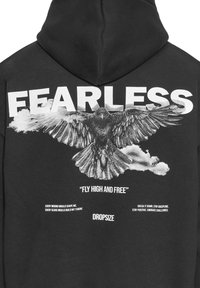 Schwarzer Hoodie mit einem großen weißen Grafiken eines fliegenden Vogels und dem Text "FREI von ANGST" darüber sowie motivierenden Sprüchen darunter.