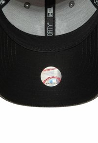 Gorra de béisbol negra con visera plana. El interior presenta una etiqueta plateada que se asemeja a una pelota de béisbol y una etiqueta con texto. Diseño de tela texturizada.