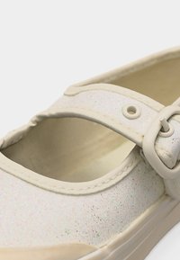 Λευκό παπούτσι Mary Jane με ιριδίζουσα γκλίτερ, ρυθμιζόμενο λουράκι και στρογγυλή πόρπη, εμφανιζόμενο σε κοντινή λήψη.