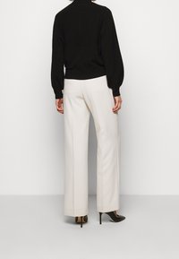 Svart tröja med hög halsringning och puffärmar, kombinerad med vita vida byxor. Svarta spetsiga klackskor fulländar outfiten.