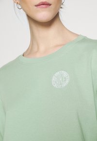 Světlezelené bavlněné tričko s kulatým výstřihem a krátkými rukávy. Na levé části hrudi má kruhové bílé logo Nike.