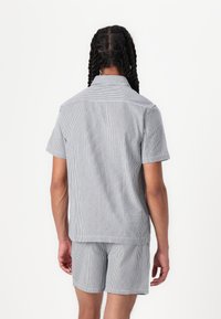 Ensemble chemise à manches courtes rayée et short bleu et blanc, avec une coupe décontractée, un tissu doux et un détail de poche subtil.