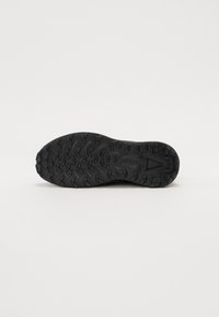 Semelle de chaussure de sport noire avec caoutchouc texturé pour une meilleure adhérence, dotée de crampons multidirectionnels et d'une zone centrale lisse.