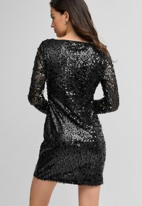 Abito nero in paillettes con maniche lunghe, dalla forma aderente e dalla texture liscia, caratterizzato da un collo a barca e una superficie scintillante.