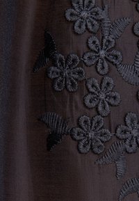 Tissu sombre et transparent avec des fleurs et des feuilles noires brodées formant un motif floral.