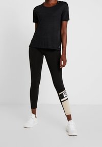 Black athletic t-shirt with a subtle striped texture, paired with black leggings featuring a tan section and white graphics. White sneakers.