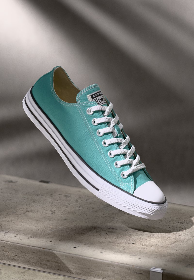 Turquoise canvas sneaker with white rubber toe cap and laces, featuring black stripe along the sole and branded tongue.