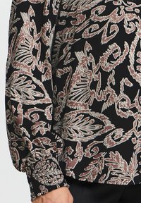 Blusa nera con motivo floreale in tonalità di marrone e crema, con polsini arricciati e una texture liscia.