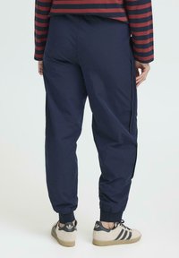 Marina joggingsbyxor med en slät yta, elastiska fotleder och detaljer i sömmarna. Bärs med beigefärgade sneakers med svarta accenter.