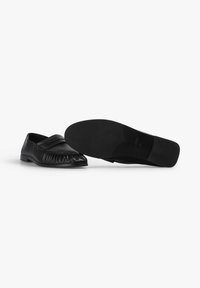 Los mocasines de cuero negro presentan una suela plana, un diseño de punta plisada y una banda ancha en la parte superior. La parte inferior tiene una superficie texturizada.