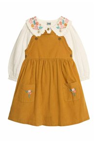 Braunes Corduroykleid mit bestickten Blumen-Taschen. Es hat eine weiße, langärmlige Bluse darunter und einen rüschierten Blumenkragen.