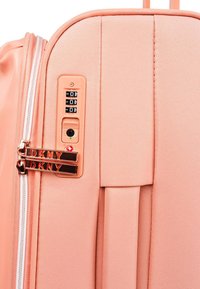 Maleta dura de melocotón con acabado texturizado, cerradura de combinación ajustable, cremalleras dobles con marca DKNY y asas de transporte lisas.