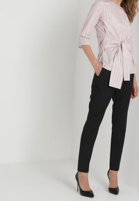 Blouse rayée rose clair à manches trois-quarts avec une taille nouée, associée à un pantalon noir ajusté et des escarpins noirs.
