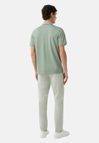 Lys grøn polo skjorte med korte ærmer, parret med lyse grå bukser og hvide sneakers. Poloen har en klassisk krave og glat tekstur.