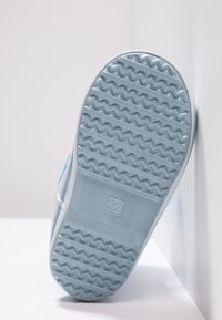 Lichtblauwe sneakerzool met een gestructureerd patroon, voorzien van zigzaggroeven voor grip. Bevat een klein "22" logo op de zool.