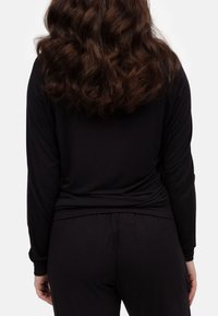 Maglietta nera a maniche lunghe con una texture liscia e design aderente, abbinata a pantaloni coordinati, entrambi realizzati in tessuto morbido e elastico.