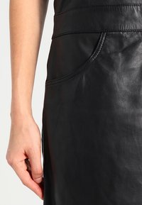 Zwarte leren rok met een gladde textuur, zijzak en gestikte details langs de taille en zoom. Close-up van het materiaal.