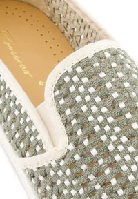 Groene geweven instapper met een lichte stofafwerking, voorzien van een textuurpatroon en een gevoerde beige binnenzool met perforaties voor ventilatie.