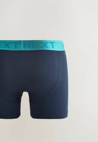 Sötétkék boxer alsónadrág puha szövetből, türkiz színű gumírozott derékkal, amin a "NEXT" logó látható. Simasága és testhezálló szabása van.