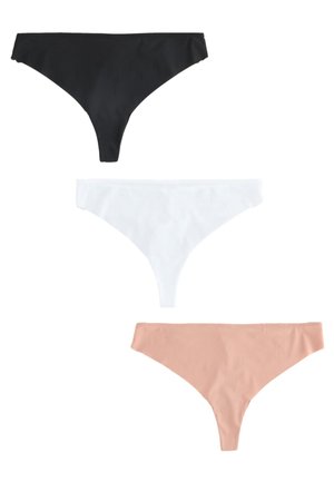 Kobieta widziana od tyłu, ubrana w cieliste stringi z koronkową lamówką i pasujący biustonosz, stojąca z jedną ręką na biodrze na jednolitym tle.