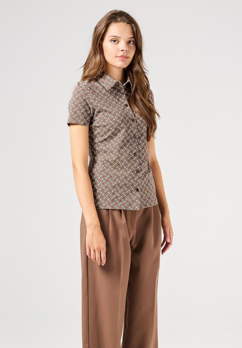 Bruine kortemouw knoopshirt met een geometrisch patroon in lichtblauw, gemaakt van lichtgewicht materiaal, gecombineerd met een bruine wijde broek.
