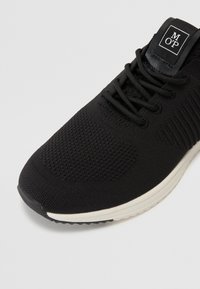 Baskets de sport noires avec un dessus en tricot respirant, motifs texturés, fermeture à lacets et une semelle blanche contrastante.