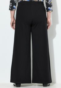 Pantalons larges noirs en tissu doux, dotés d'une taille élastique et d'une finition lisse et propre. La silhouette est décontractée et moderne.
