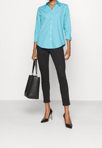 Turkos, långärmad skjorta med vita vertikala ränder, matchad med svarta slim fit-byxor och svarta klackskor. Inkluderar en svart handväska.