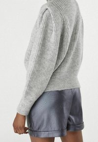 Grå stickad tröja med ribbad textur, parat med glänsande mörkgrå lädershorts med vikta fållar. Bakvy av outfiten.