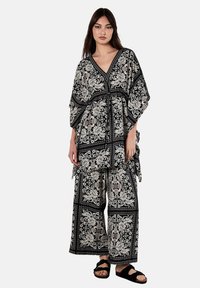 Schwarz-weißes Blumenmuster-Outfit mit einem locker sitzenden Oberteil mit V-Ausschnitt und weiten Hosen. Strukturierter Stoff mit einem insgesamt fließenden Design.