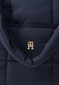 Granatowa ocieplana torba na ramię o pikowanej fakturze, z złotym logo z przodu i materiałowym paskiem do noszenia.