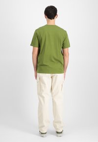 Grøn bomulds t-shirt med korte ærmer, parret med cremede cargo bukser med sidelommer og en afslappet pasform. Bagfra vist.