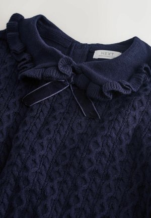 Granatowy sweter dziewiarski z falbaniastym kołnierzem, z detalem w postaci kokardy. Teksturowany wzór w warkocz i miękka tkanina.