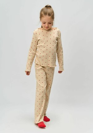 Beige geribde pyjama set met rode hartpatronen, lange mouwen top met geschulpte halslijn, bijpassende broek met rafelige randen, gecombineerd met rode schoeisel.